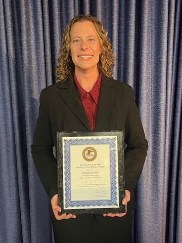 DCAA Operations Investigative Support Auditor Pam Kochis standing in front of a blue curtain holding an award.