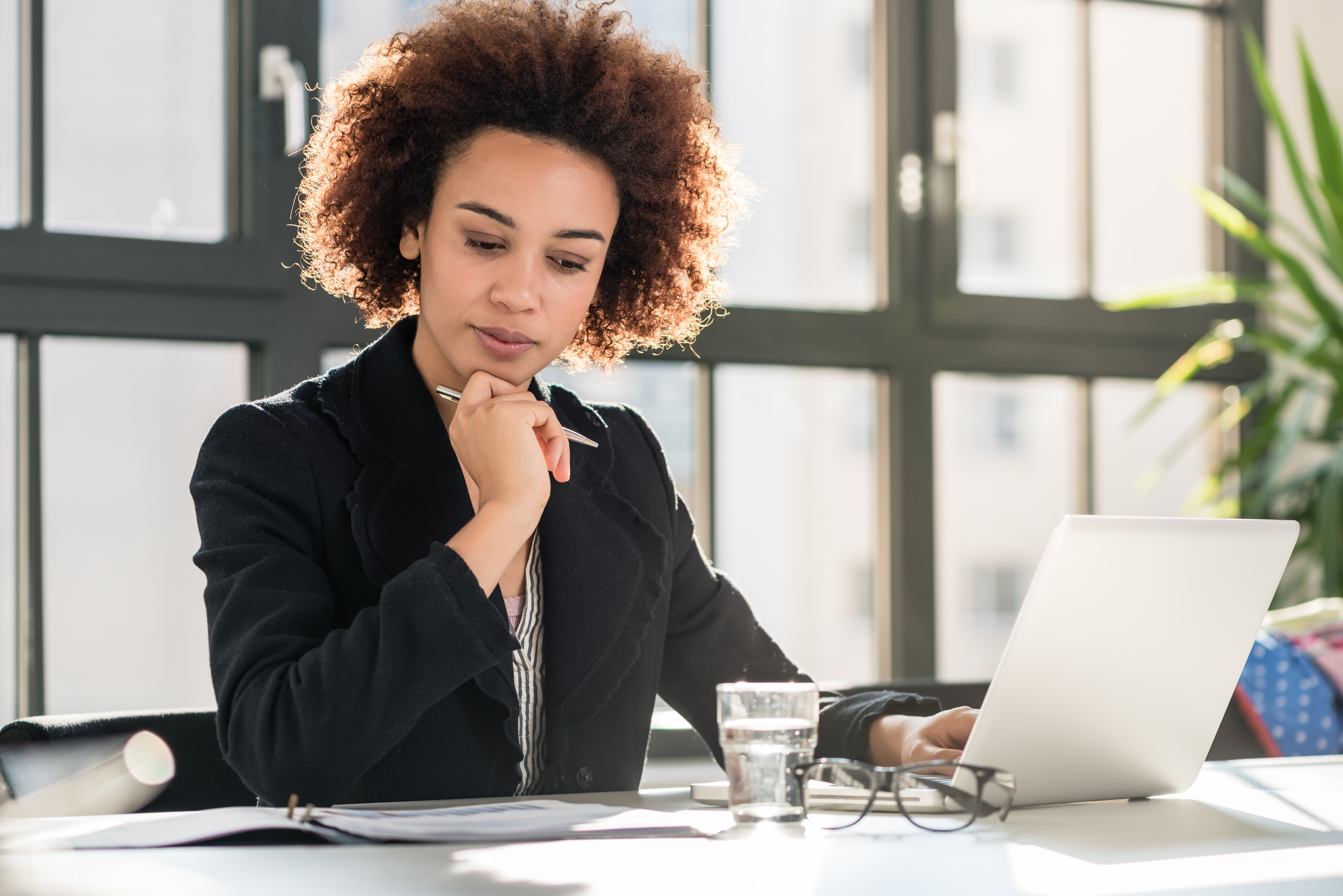 Young black lady sitting in a office holding a pencil and looking at a notebook. Young black lady sitting in a office holding a pencil and looking at a notebook.