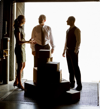 Three employees standing in a warehouse next to boxes. 