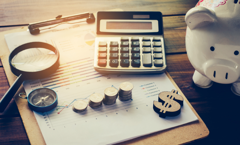 Calculator, magnifying glass, piggy bank, and clipboard on a wooden table.